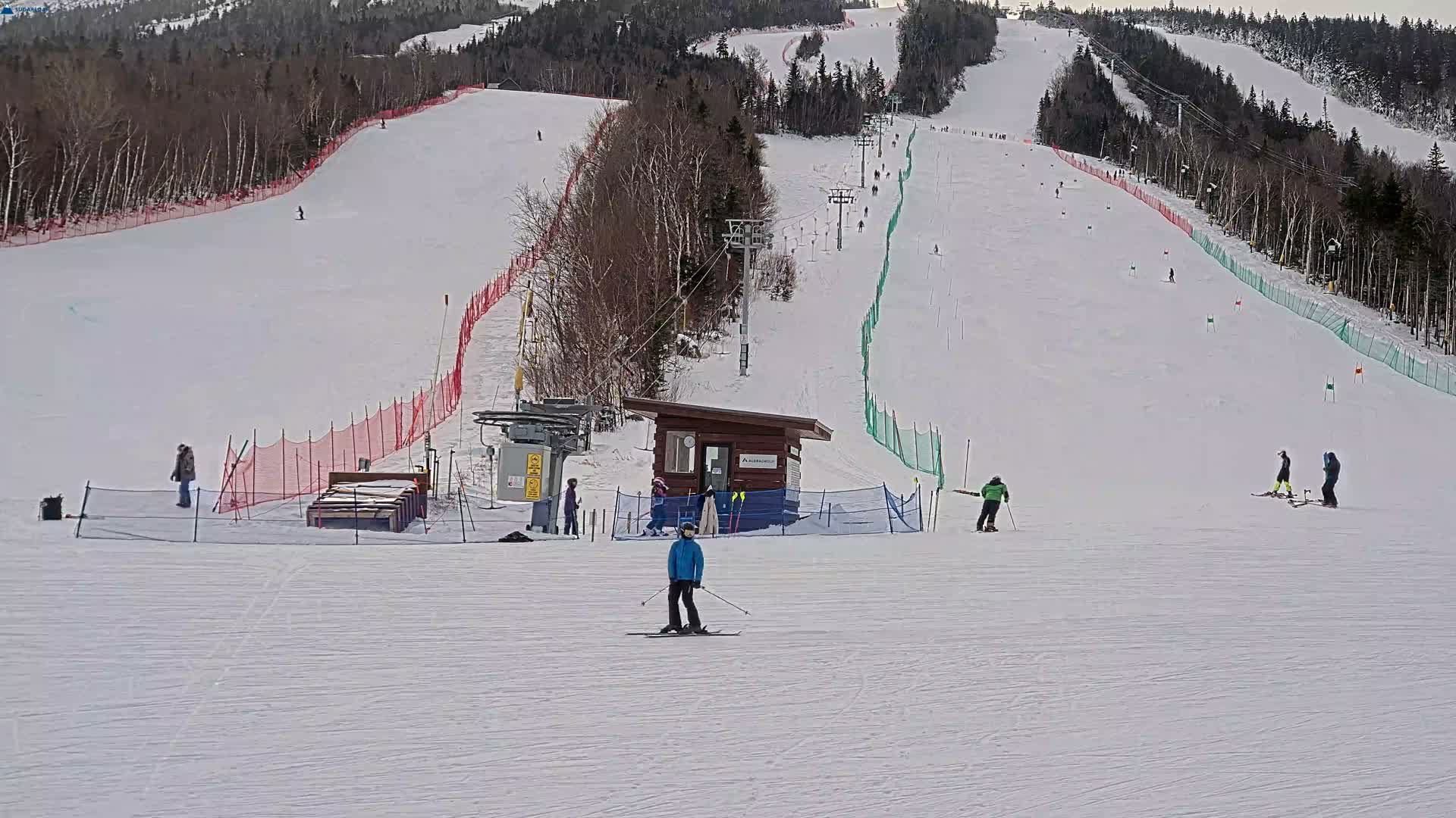 A snowy ski slope is brightly illuminated by artificial lights at night, revealing groomed snow, active snowmaking equipment, and a clear, cold sky.