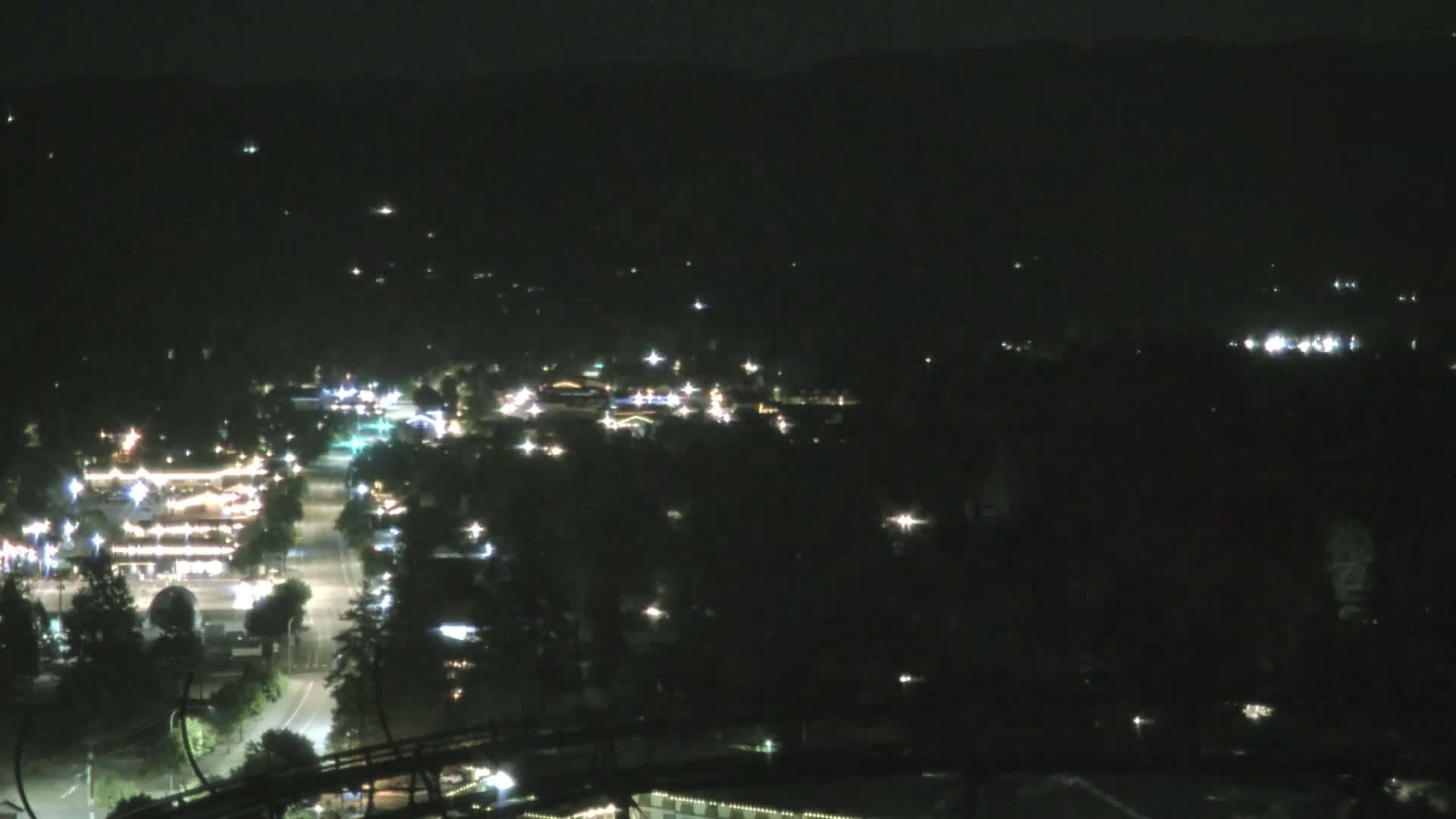 A nighttime, high-angle view shows a small town nestled in a valley, illuminated by scattered lights.