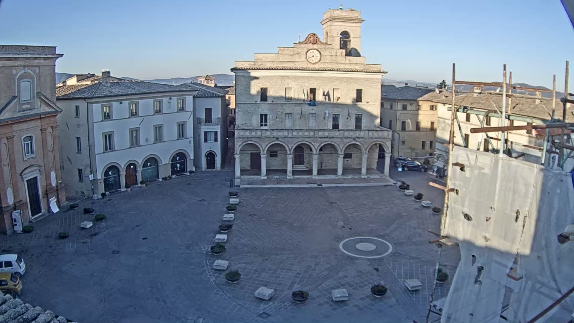 A large, empty town square is surrounded by historic buildings under a clear, sunny sky.
