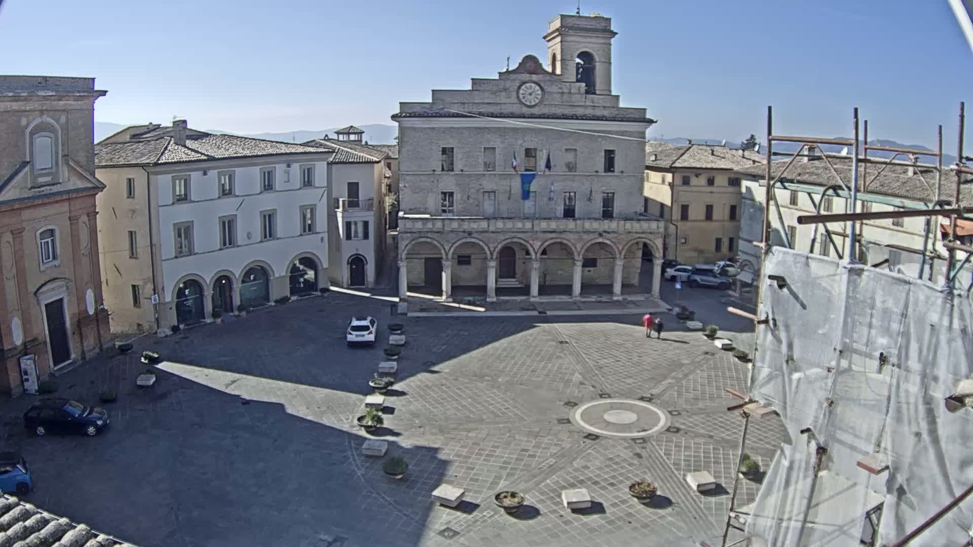 A large town square with a prominent stone building, surrounded by other buildings, on a sunny day.