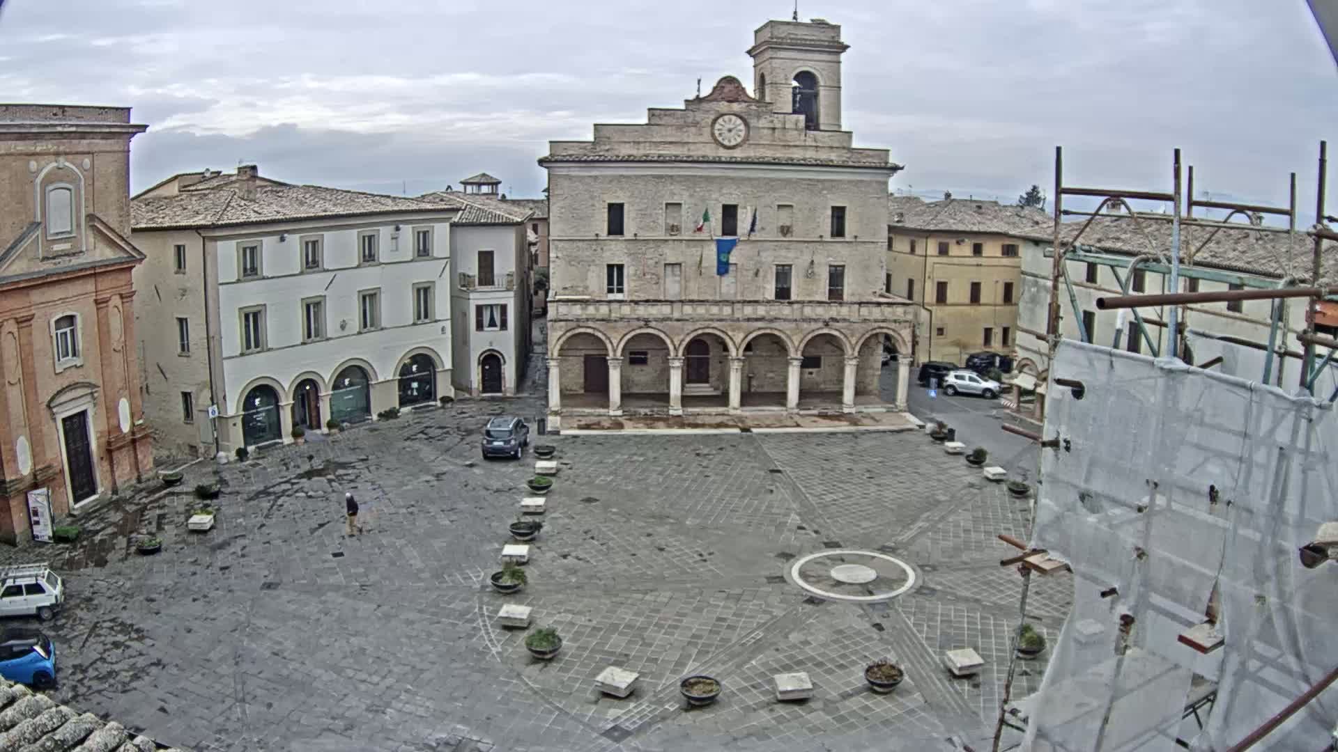A large, mostly empty town square with several buildings surrounding it, under an overcast sky.