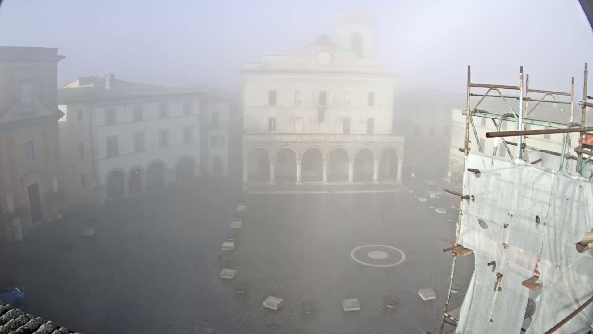 A foggy town square is seen from above, featuring several buildings and construction scaffolding.