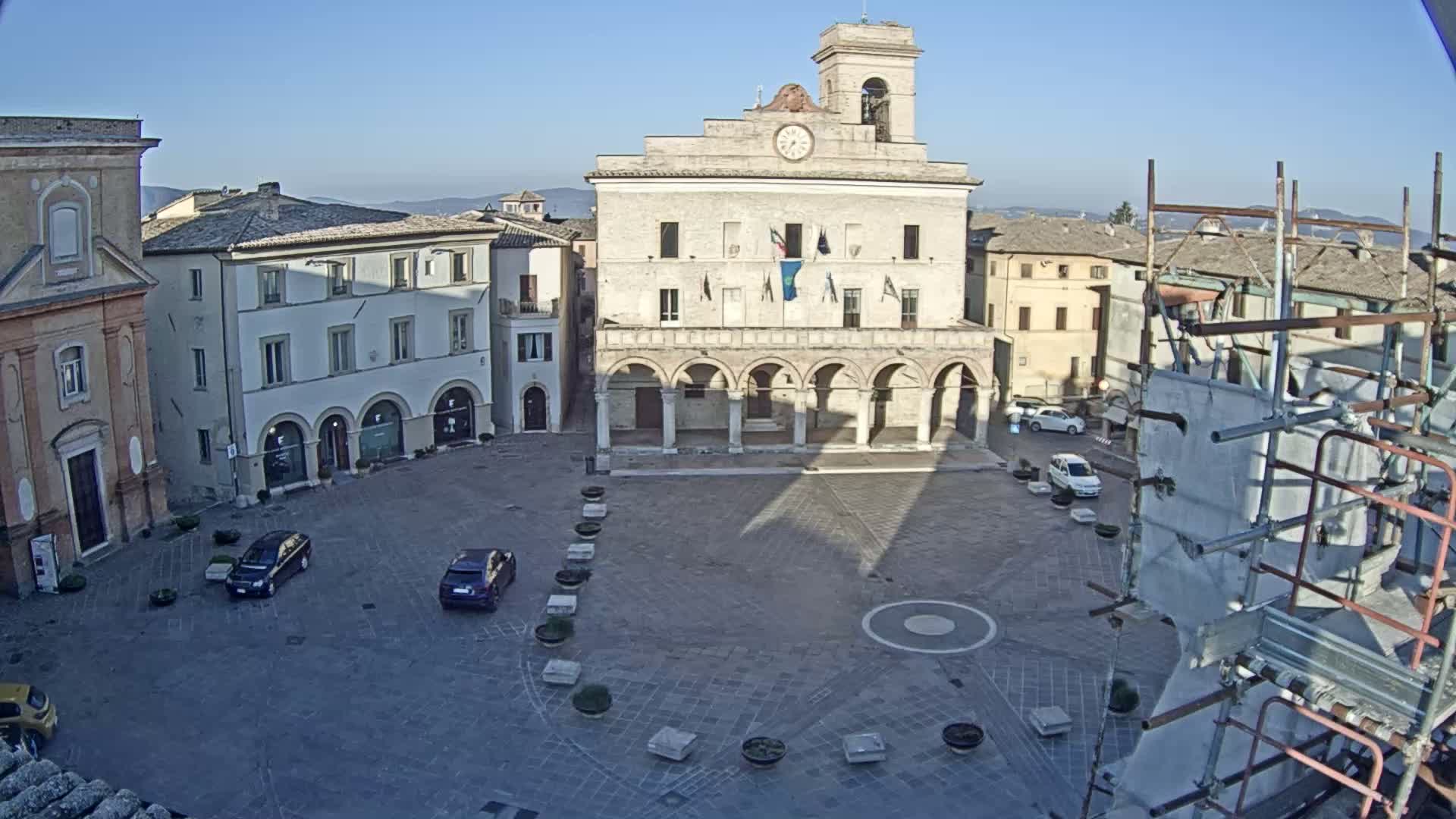 A town square with a large stone building and a few parked cars, under a clear blue sky.