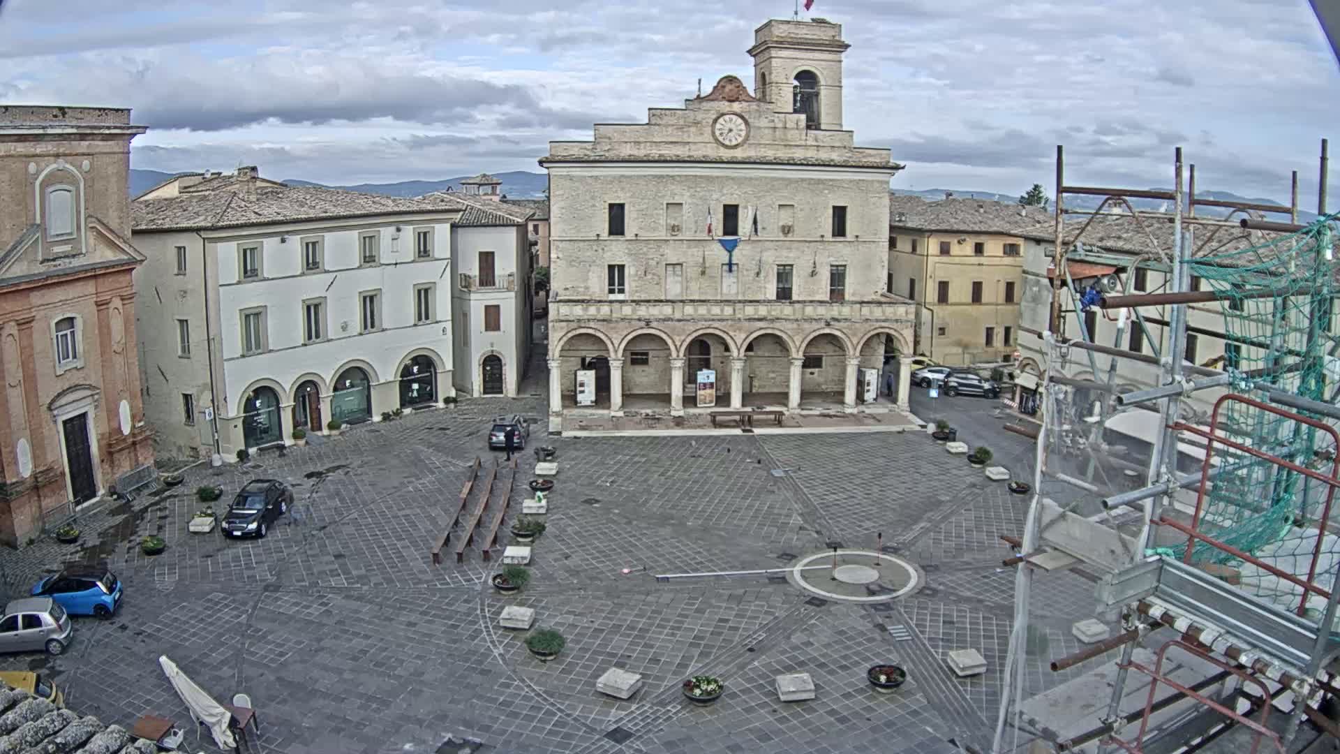 A mostly empty town square with a large stone building in the center, surrounded by other buildings, under an overcast sky.