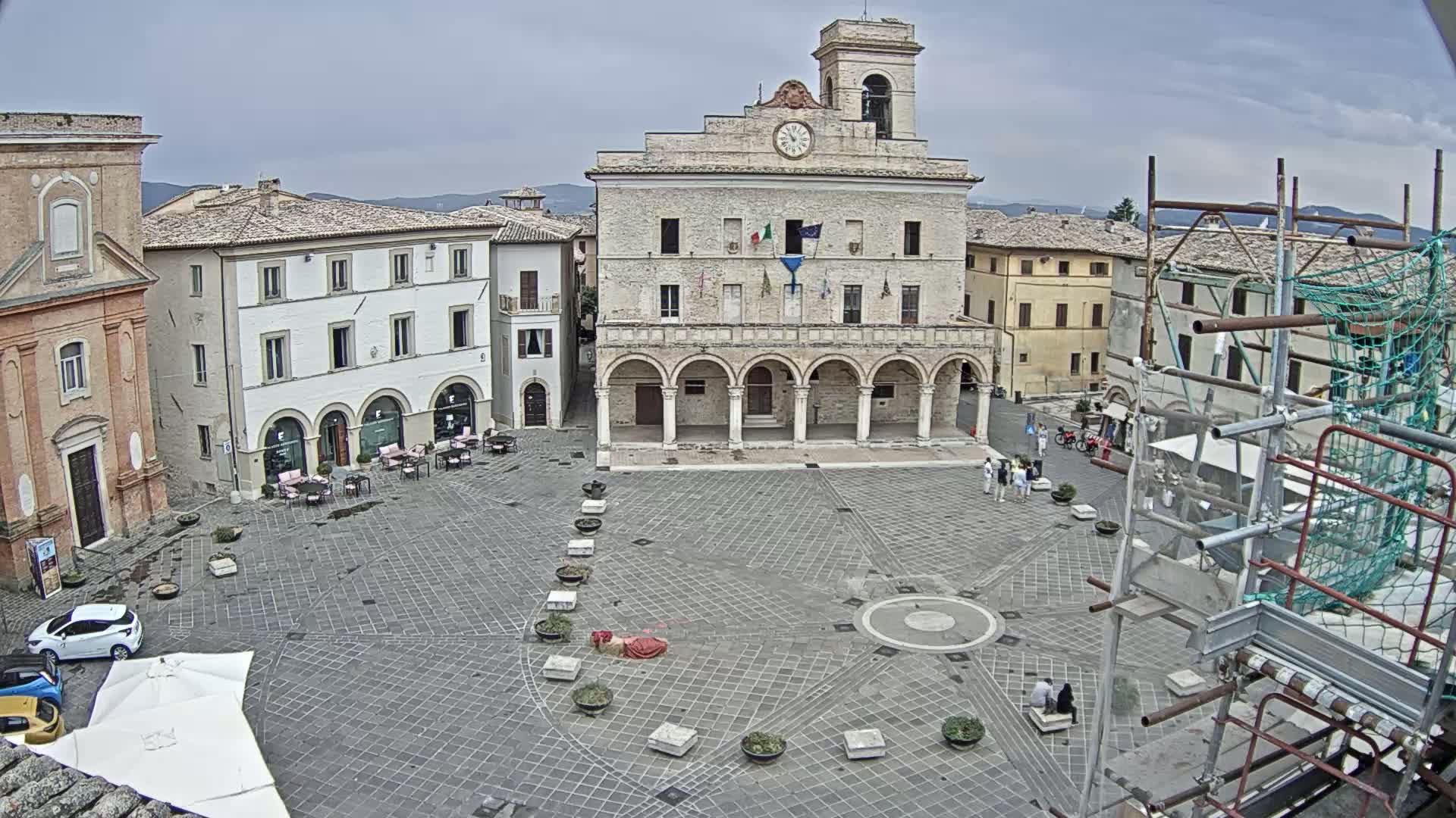A town square with a large stone building, surrounded by other buildings, under an overcast sky.