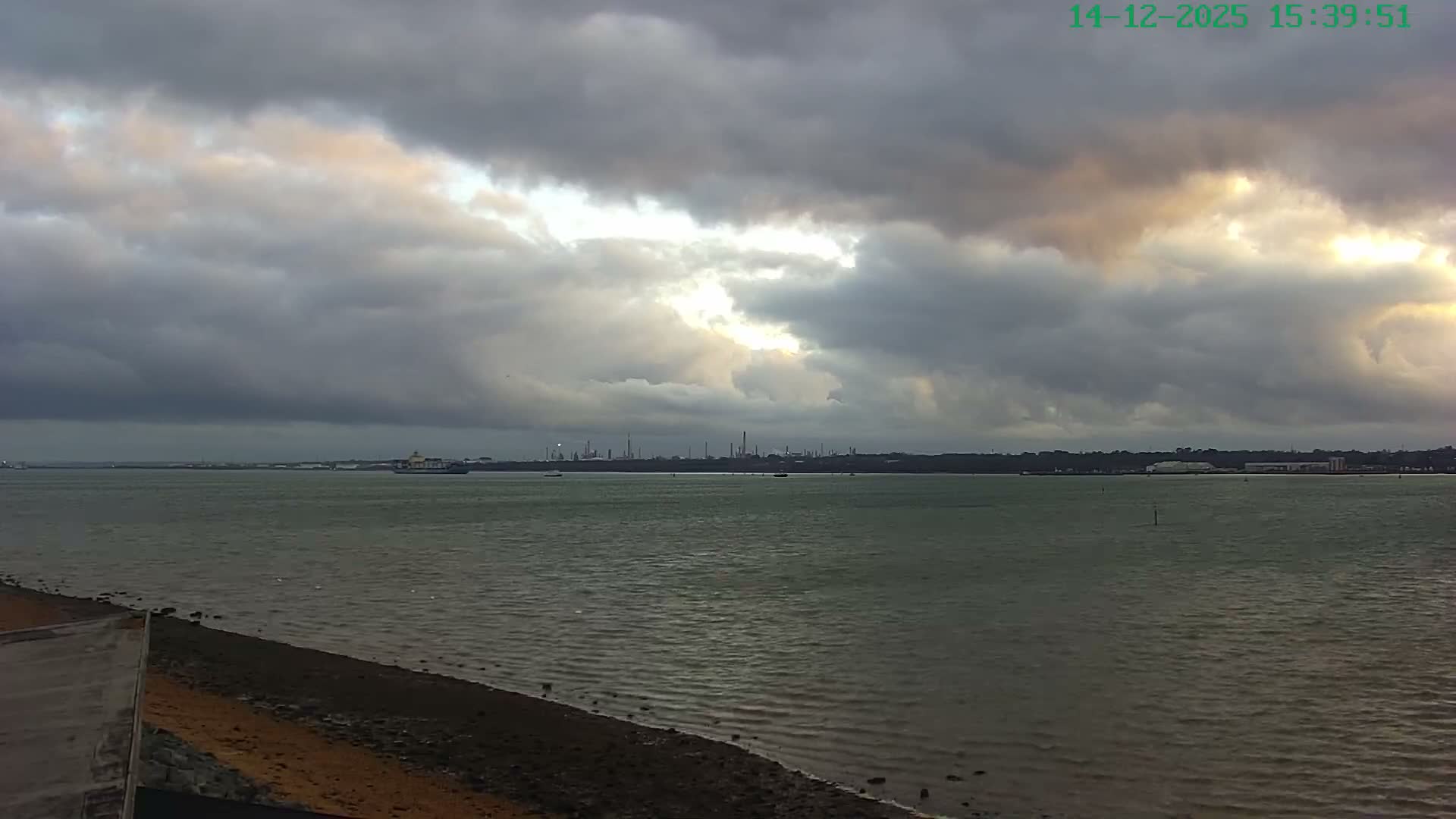A large blue and white car carrier is docked at a port under an overcast sky, with a ramp connecting to a multi-story car park filled with vehicles.