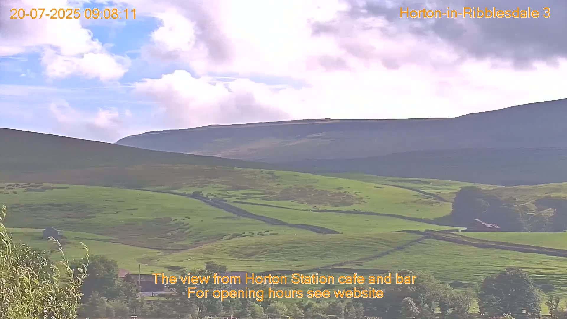 Rolling green hills and distant mountains are visible under a partly cloudy sky.
