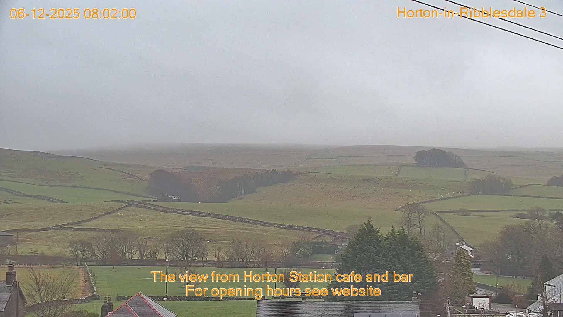 A vast, misty landscape of rolling green and brown hills, segmented by numerous stone walls and dotted with scattered trees and distant structures, is visible under a uniformly overcast sky.