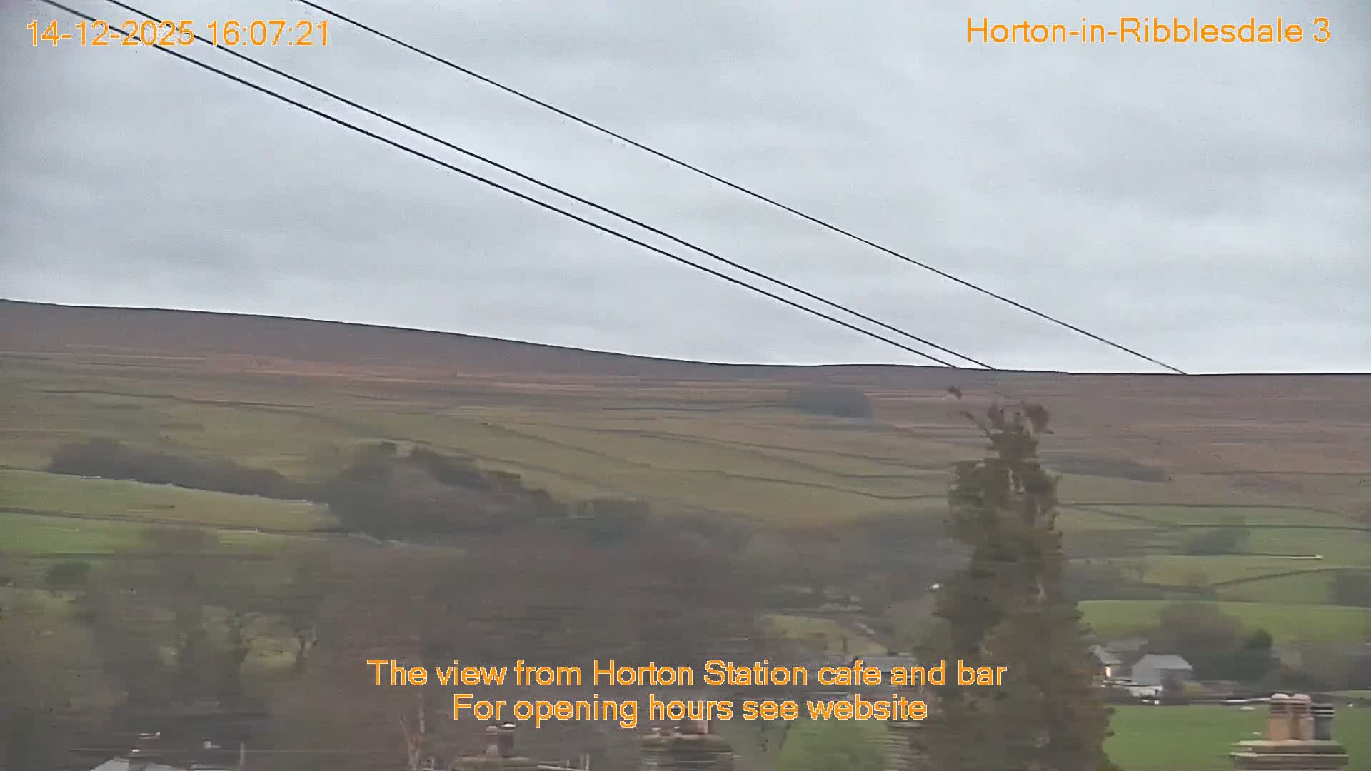 A vast, misty landscape of rolling green and brown hills, segmented by numerous stone walls and dotted with scattered trees and distant structures, is visible under a uniformly overcast sky.