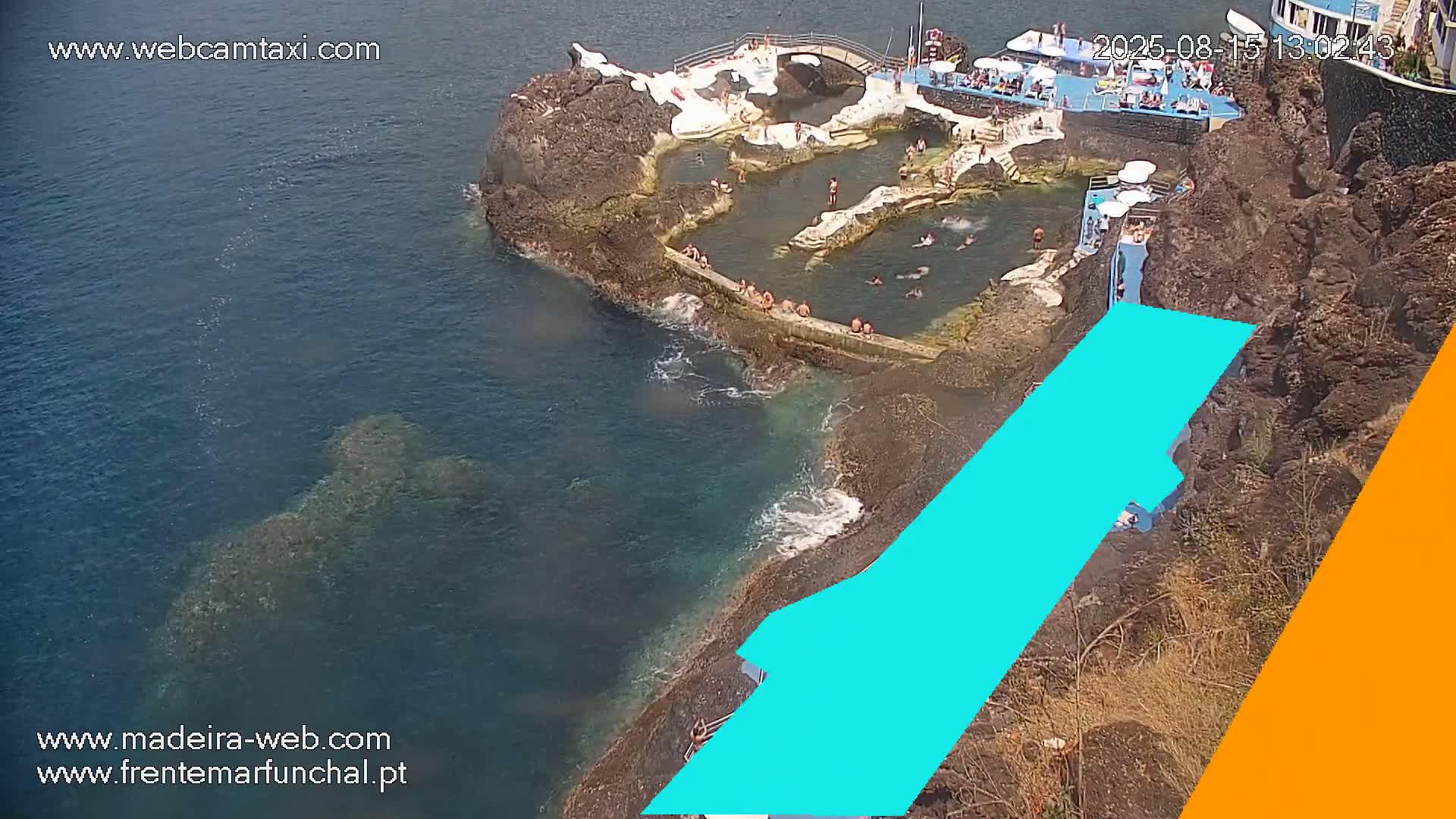 An aerial view shows a rocky coastal area with a man-made pool complex and a circular building, all under hazy or overcast conditions.