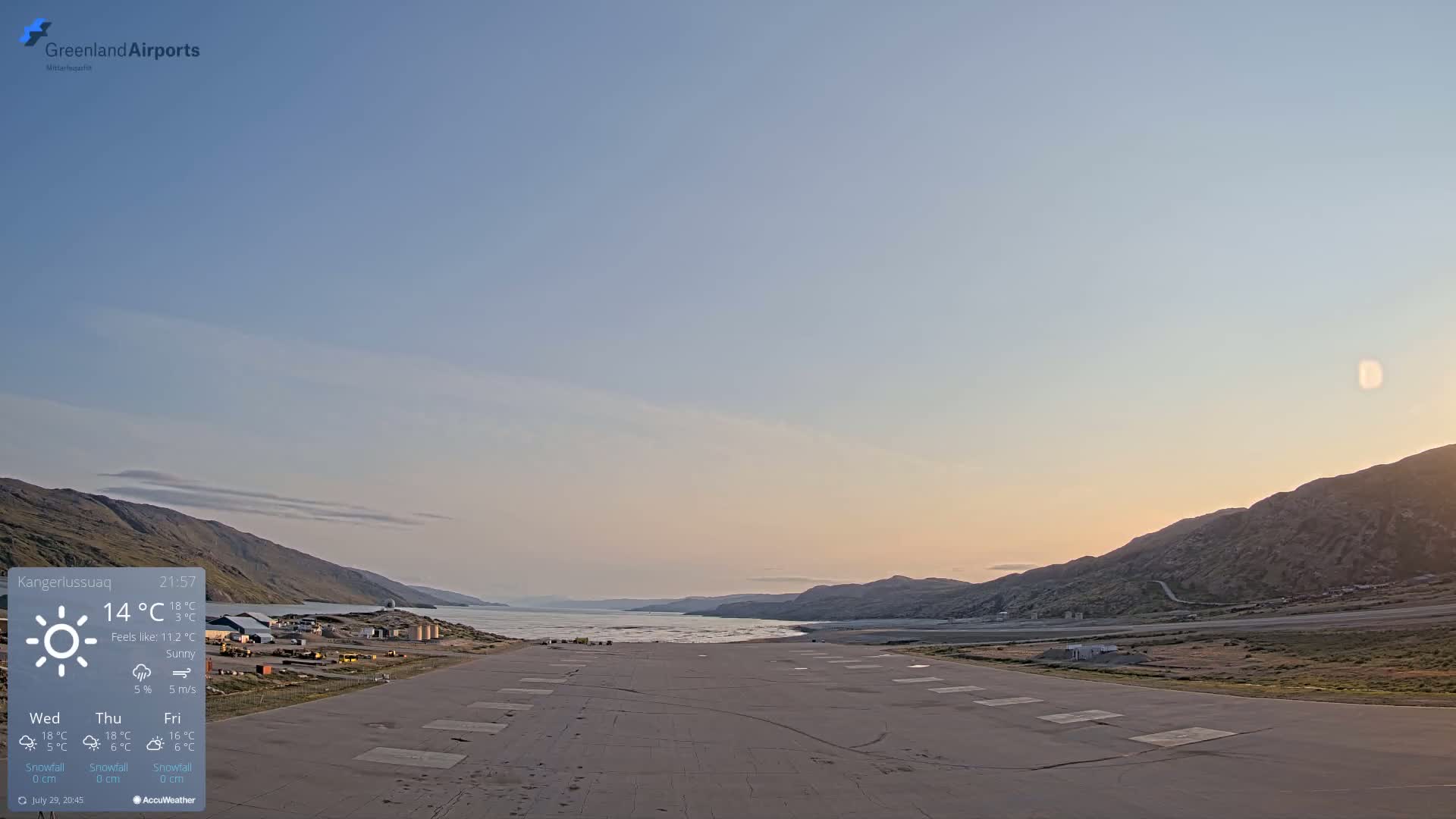 A wet, gray airstrip is visible, with low-lying clouds and fog obscuring distant mountains under a drizzle.