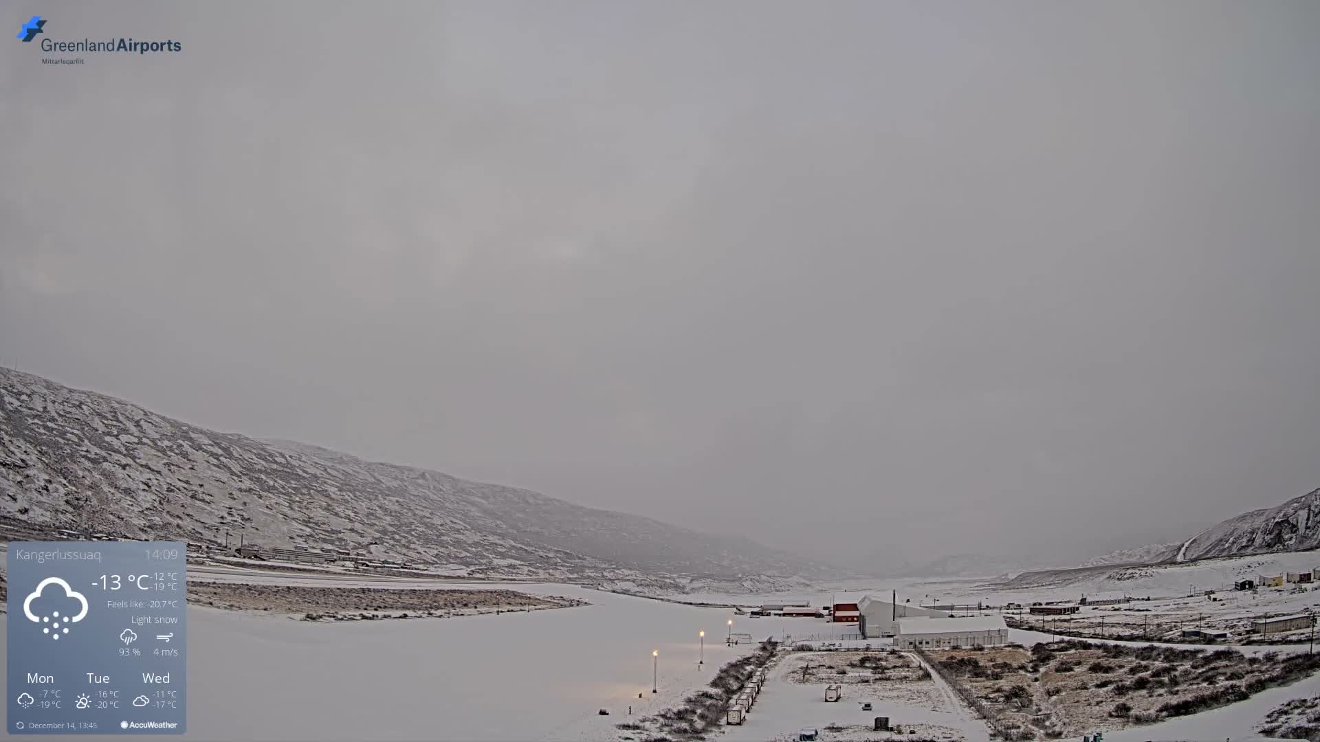 A clear, cold night reveals shimmering green aurora borealis over a snow-covered arctic landscape featuring a brightly lit airport runway and adjacent buildings.