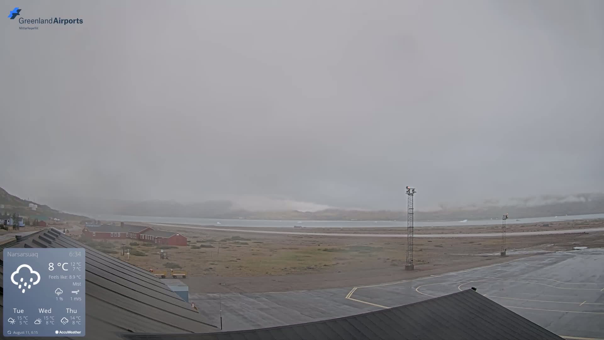 A misty, rainy scene shows an airport runway, buildings, and a body of water with some icebergs visible in the distance.