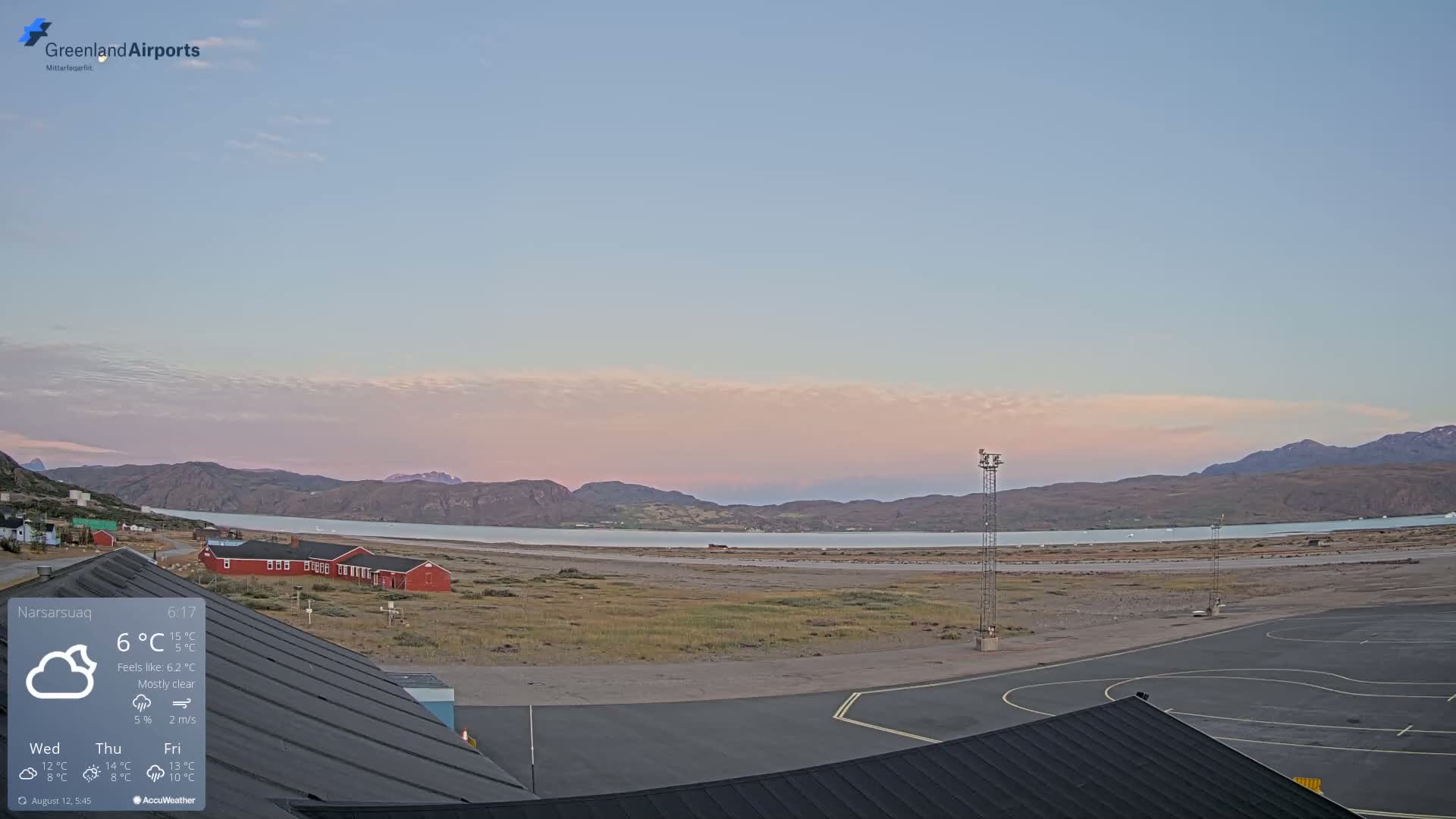A mostly clear, twilight sky over a small airport near water, with low mountains in the background.