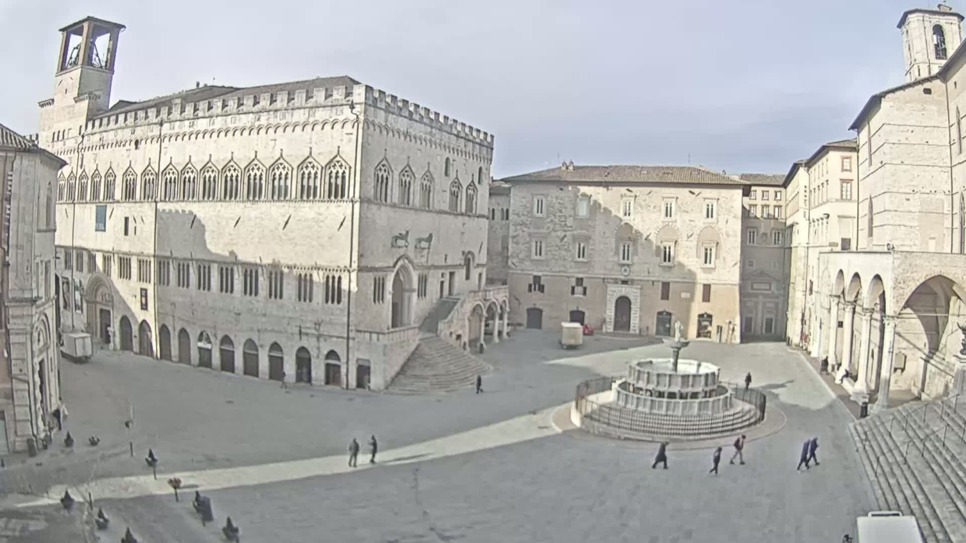 A large, mostly empty town square with several stone buildings surrounding it, under a clear sky.