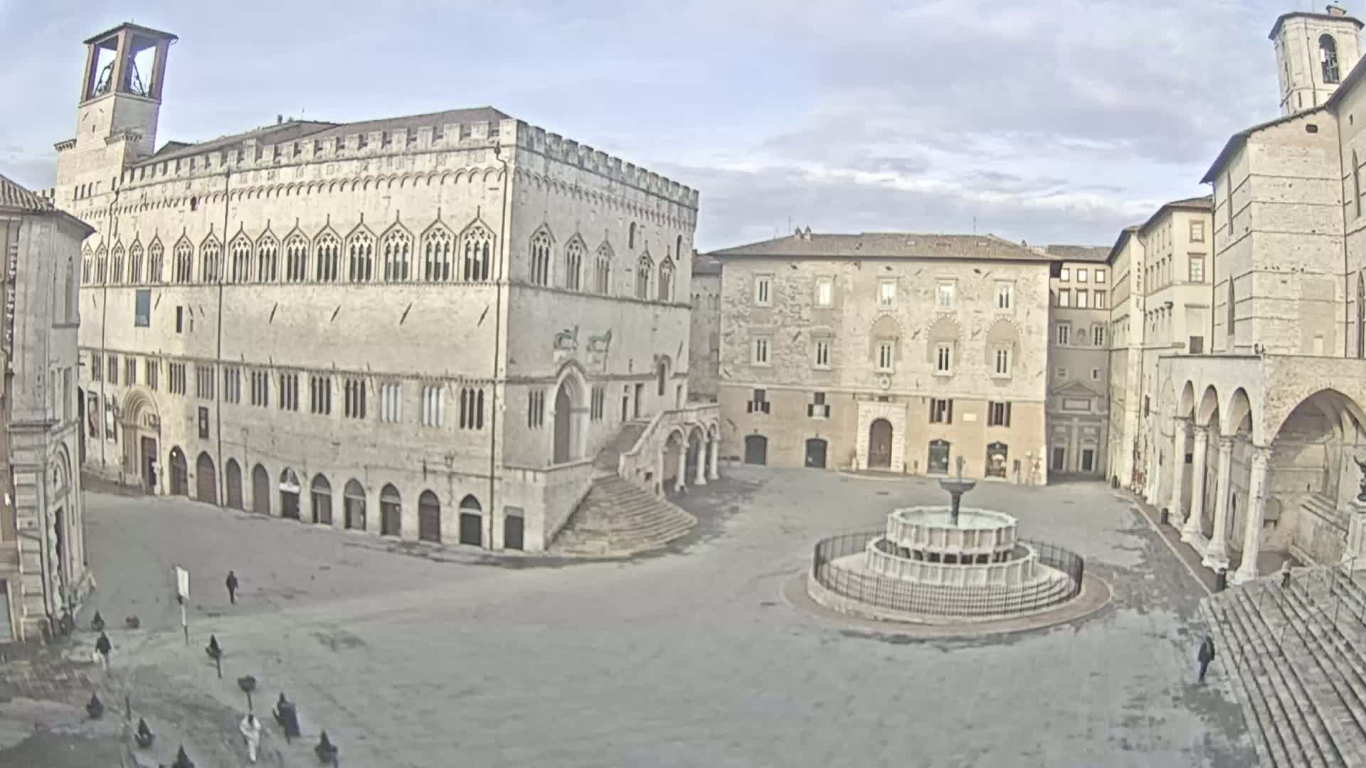 A large, mostly empty town square is surrounded by several light-colored stone buildings under an overcast sky.