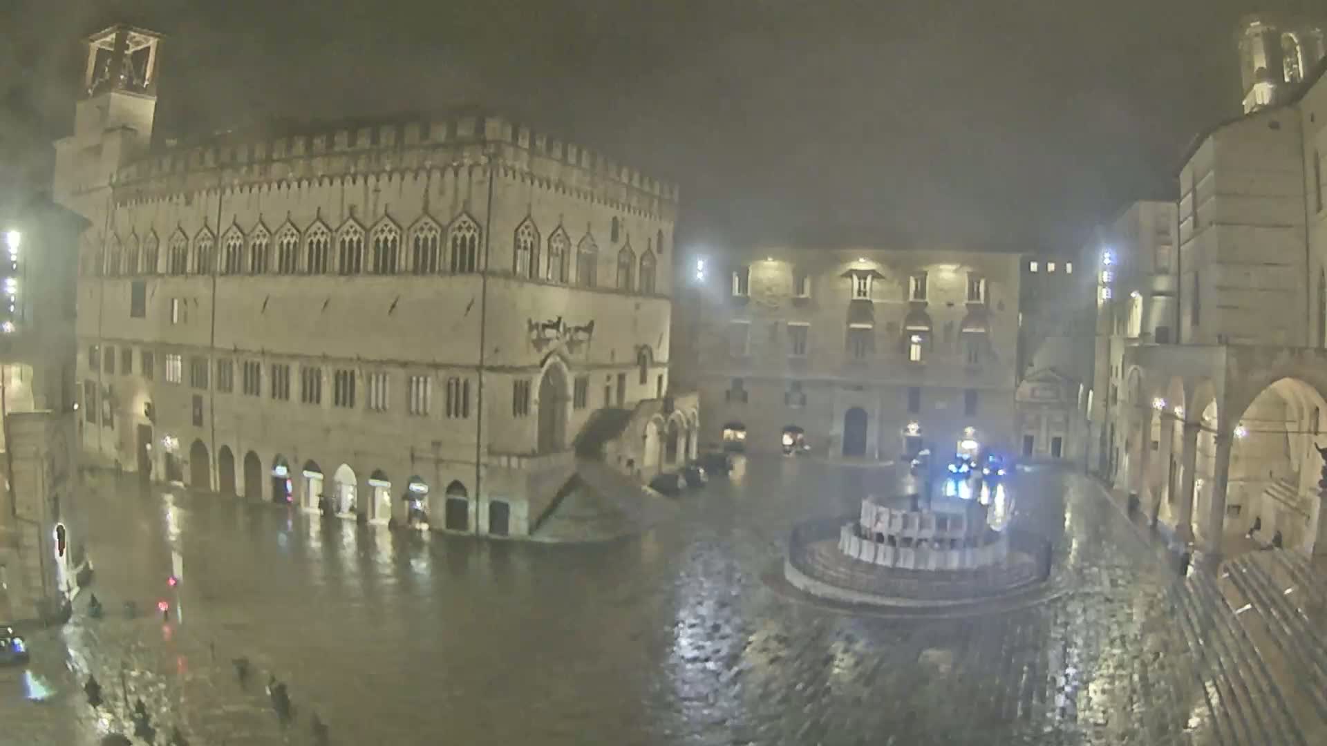 A large, flood-covered town square at night, surrounded by historic stone buildings under heavy rain.