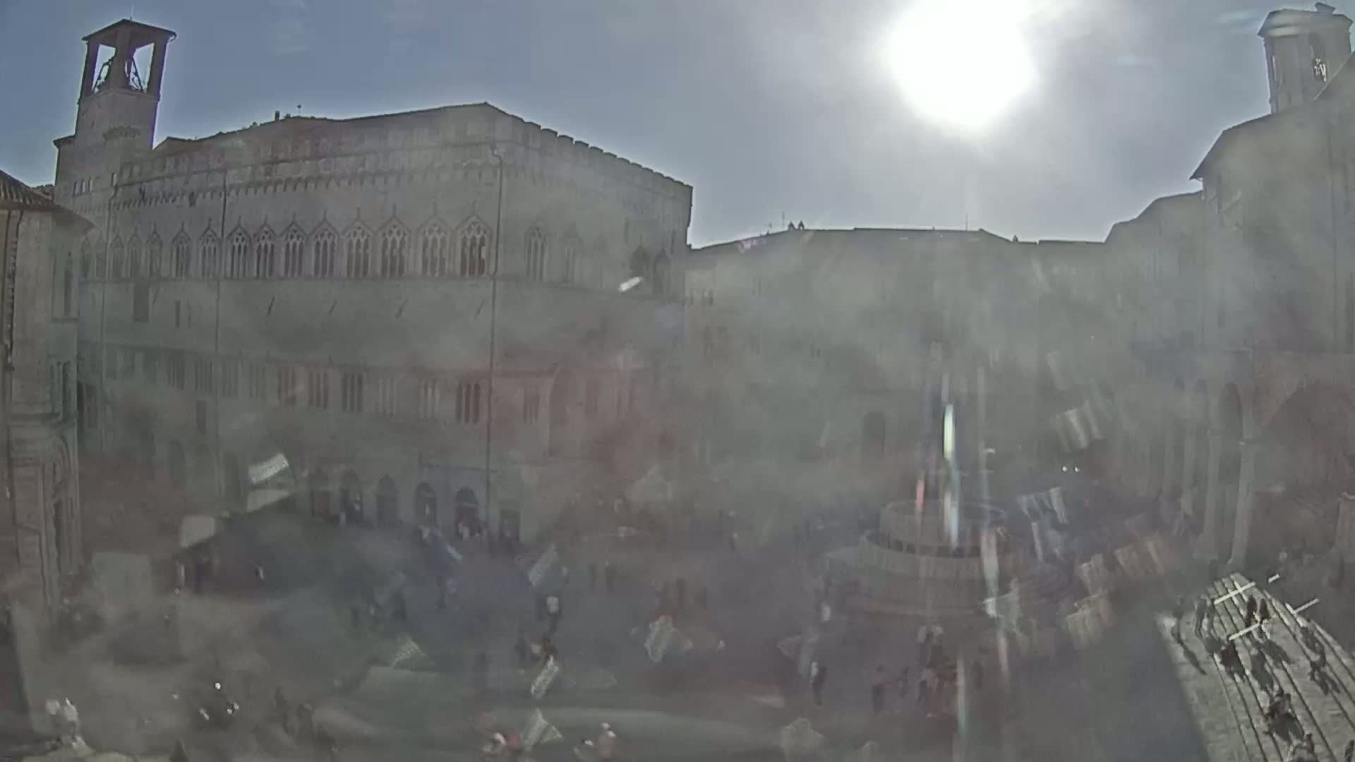 A sunny day reveals a large, stone public square surrounded by old buildings, with many people scattered throughout.