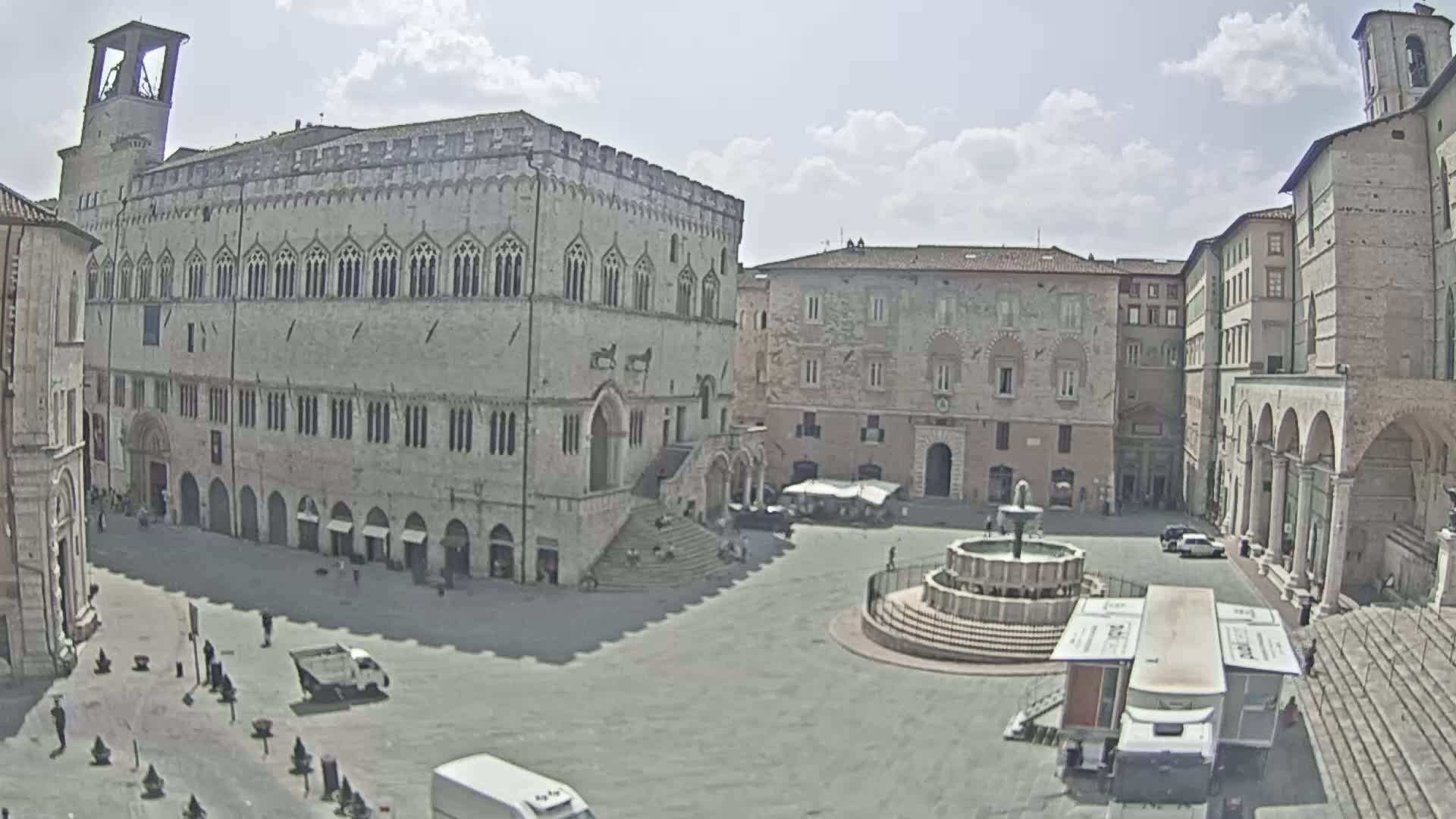 A large, mostly empty town square is surrounded by aged stone buildings, including a prominent palace, under a partly cloudy sky.