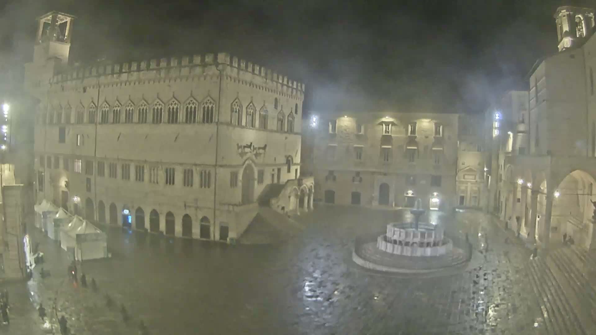 A bustling historic city square is viewed under a cloudy sky, surrounded by ornate stone buildings and a prominent bell tower, with market tents and a multi-tiered fountain amidst a large crowd of people.