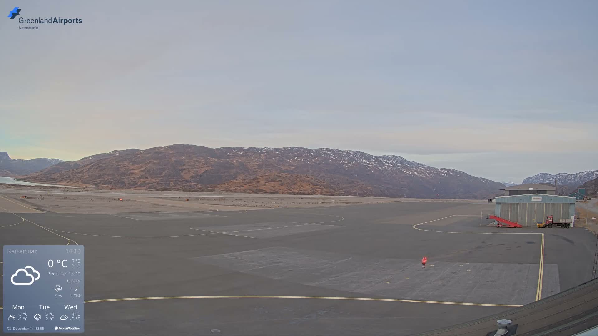 A clear, cold night reveals an airport runway and a hangar framed by snow-dusted mountains and a starry sky.