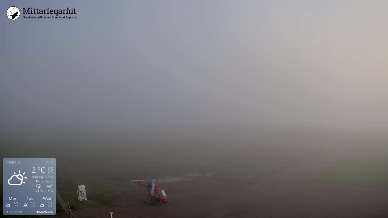 A red helicopter sits on a foggy airfield.