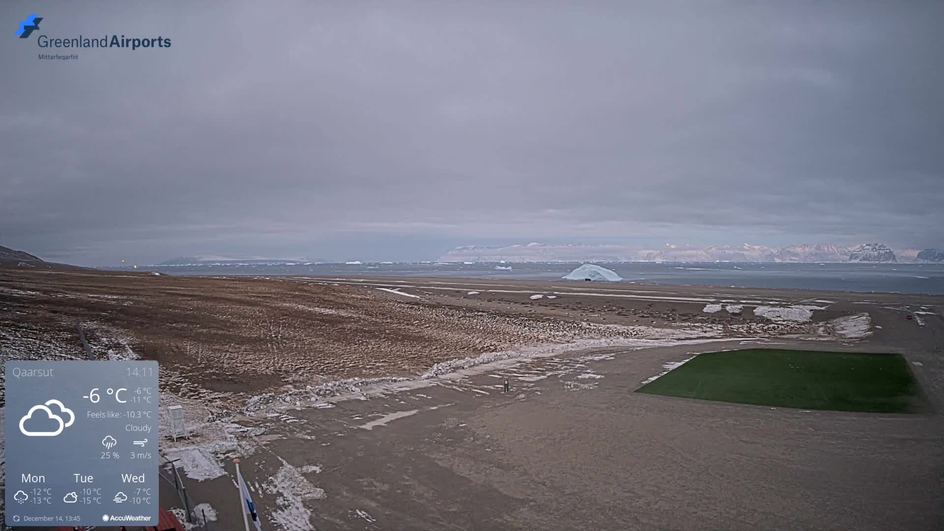 The image displays a vast, dark, snow and ice-covered landscape with distant airfield lights, a solitary person, and a body of water featuring an iceberg, all set against a backdrop of snow-capped mountains under a cold, overcast sky.
