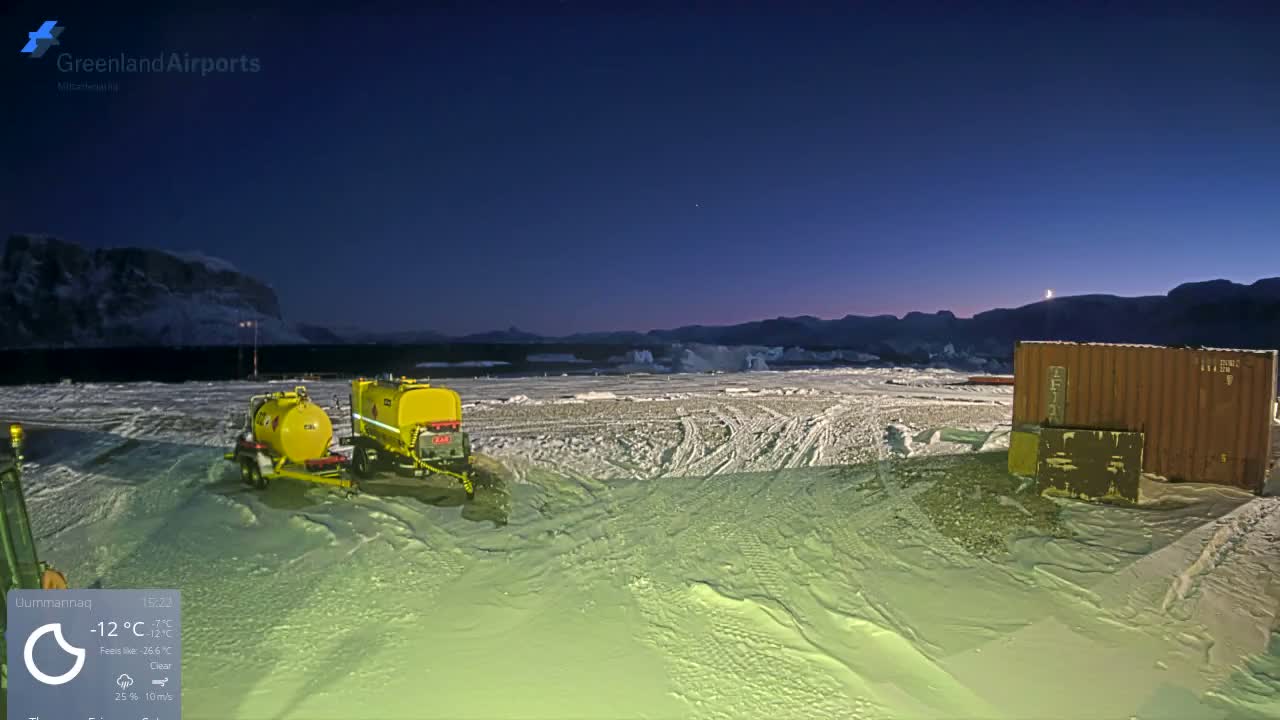 A clear, cold, snowy night reveals two yellow tanker trailers and a brown shipping container on a snow-covered field, with distant ice formations visible under a dark sky.