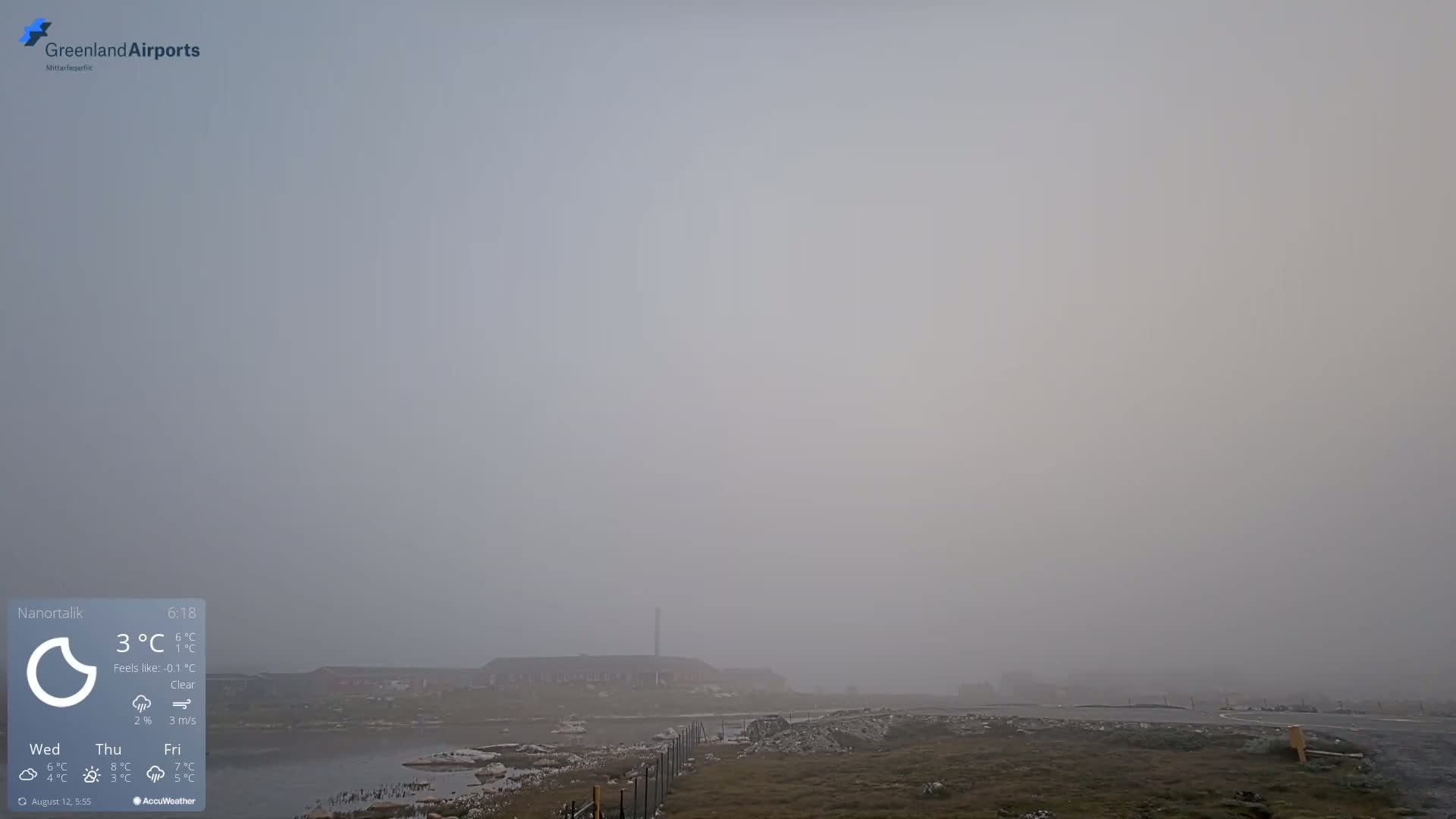A foggy, flat landscape with a body of water and a few buildings in the distance is visible under a gray sky.