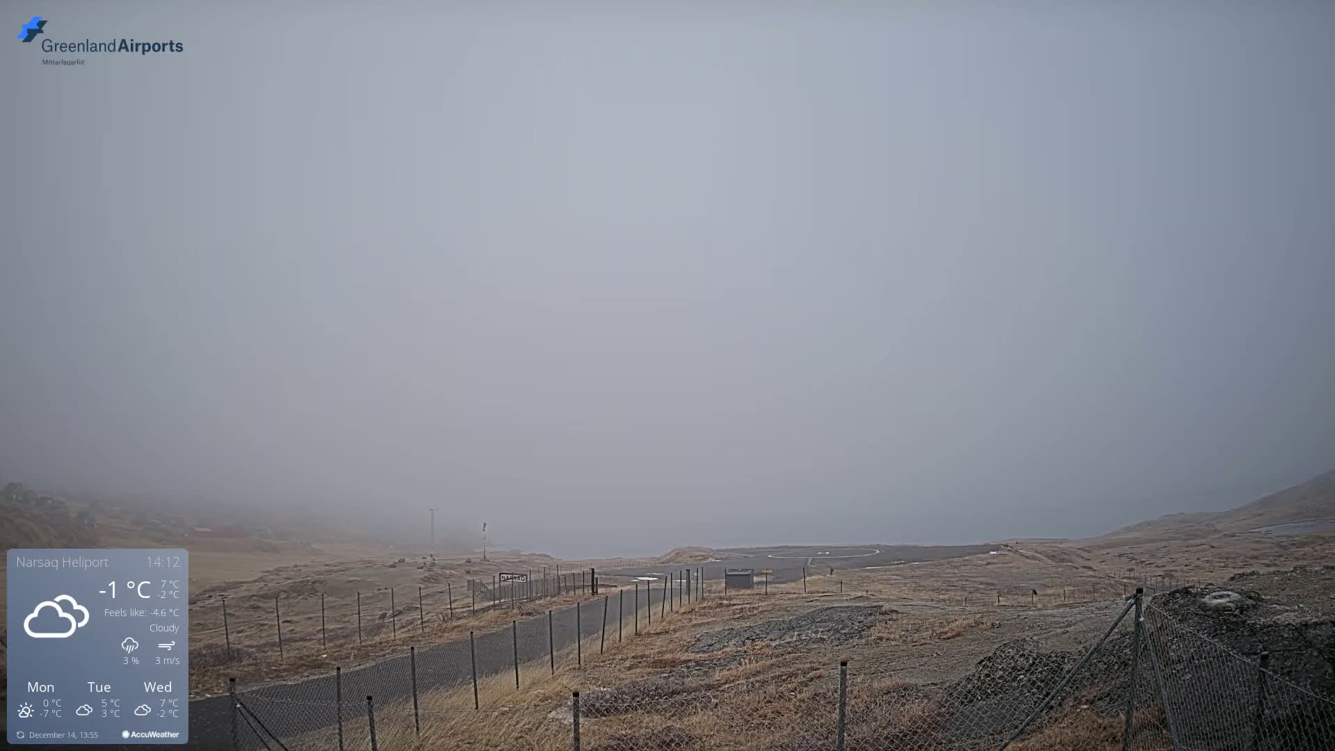 A clear night sky with visible stars and a prominent moonbeam illuminates a landscape featuring a small, lit-up settlement nestled among snow-capped mountains, a body of water, and a snowy field with a chain-link fence in the foreground.