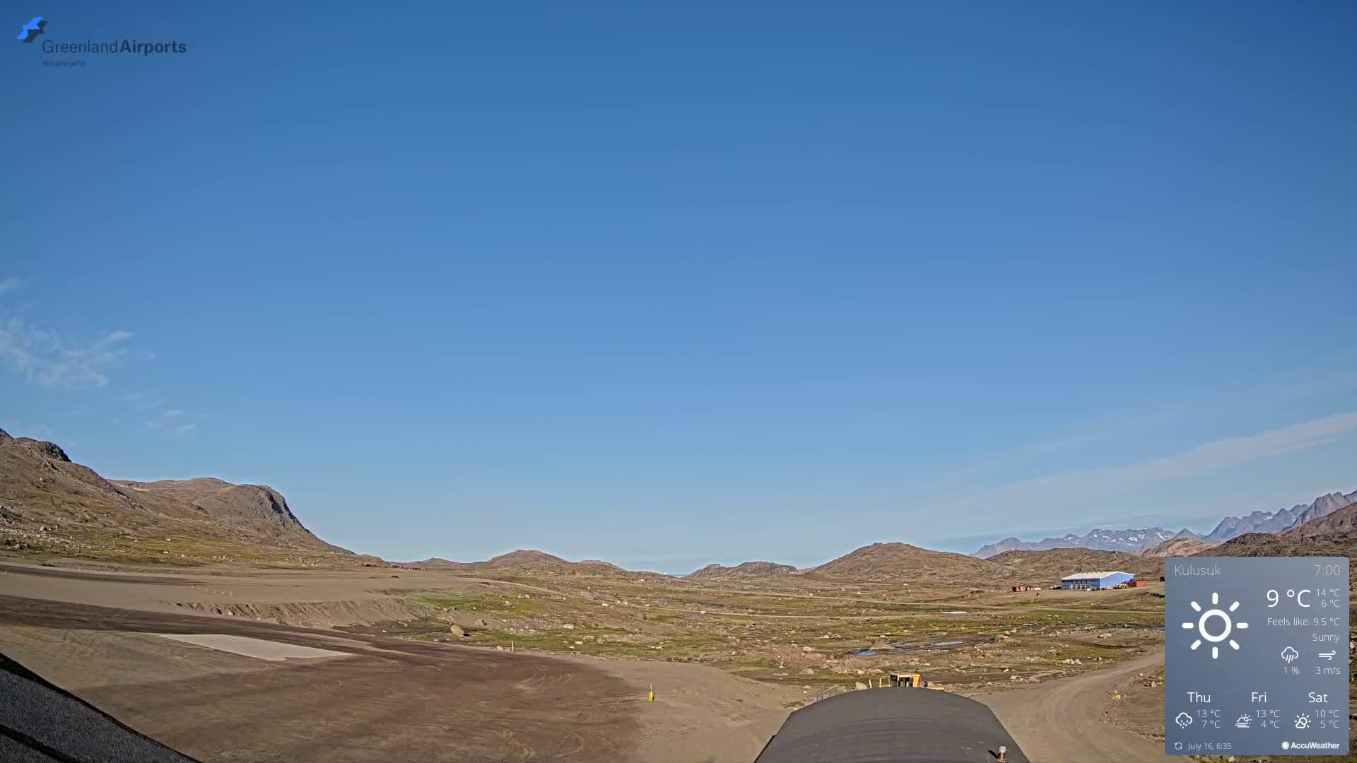 A flat, barren landscape under a clear blue sky, with low-lying brown hills in the distance.