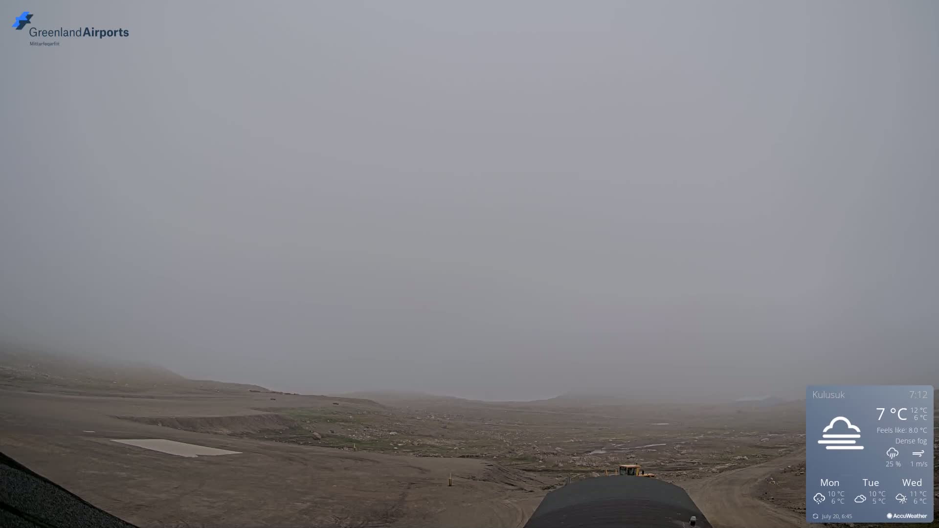 A flat, barren landscape is shrouded in dense fog, with some construction equipment visible in the foreground.
