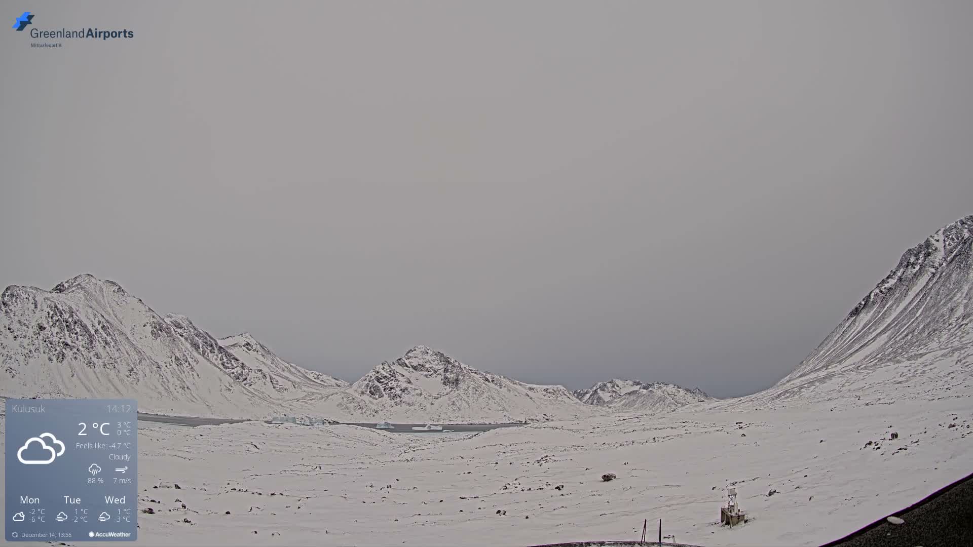 A vast, desolate, snow-covered mountainous landscape is visible under a dim, mostly cloudy sky, with bright artificial lights illuminating a distant area.