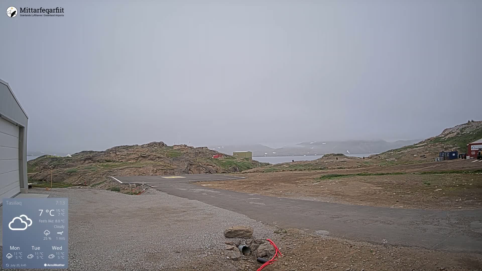 A small airport tarmac with a cloudy, foggy sky and rocky, barren hills in the background.