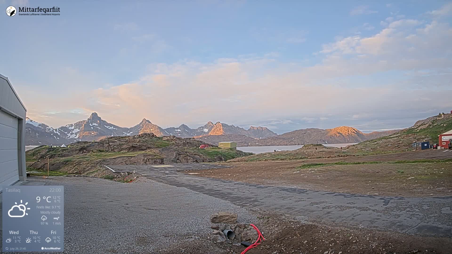 A small airport tarmac with a cloudy, foggy sky and rocky, barren hills in the background.