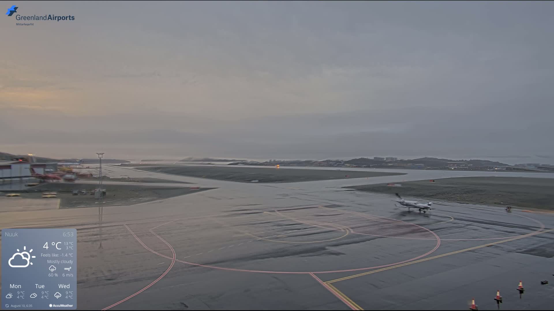 A small airplane taxis on a wet airport tarmac under a mostly cloudy, gray sky.
