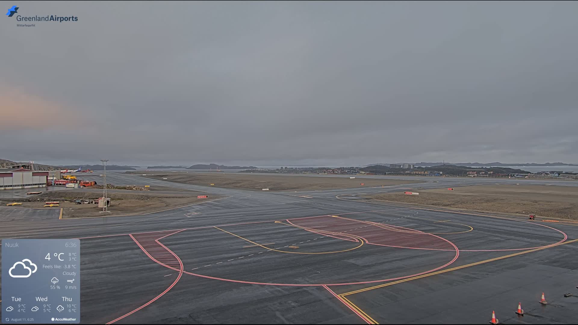 A cloudy, overcast day at an airport with tarmac markings visible, showing a small town in the distance.