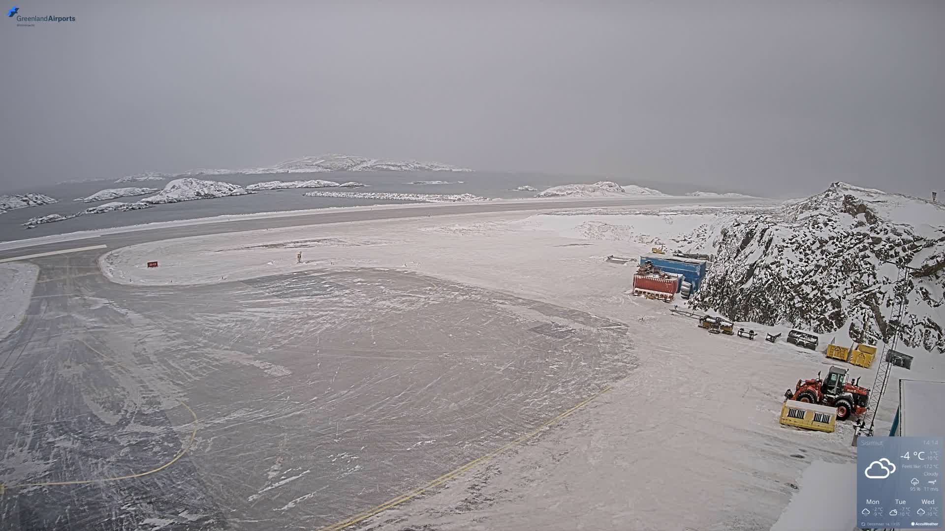 The image depicts a snowy, cold night scene at what appears to be an arctic airport or industrial site next to a body of water with islands, under a clear, star-filled sky.