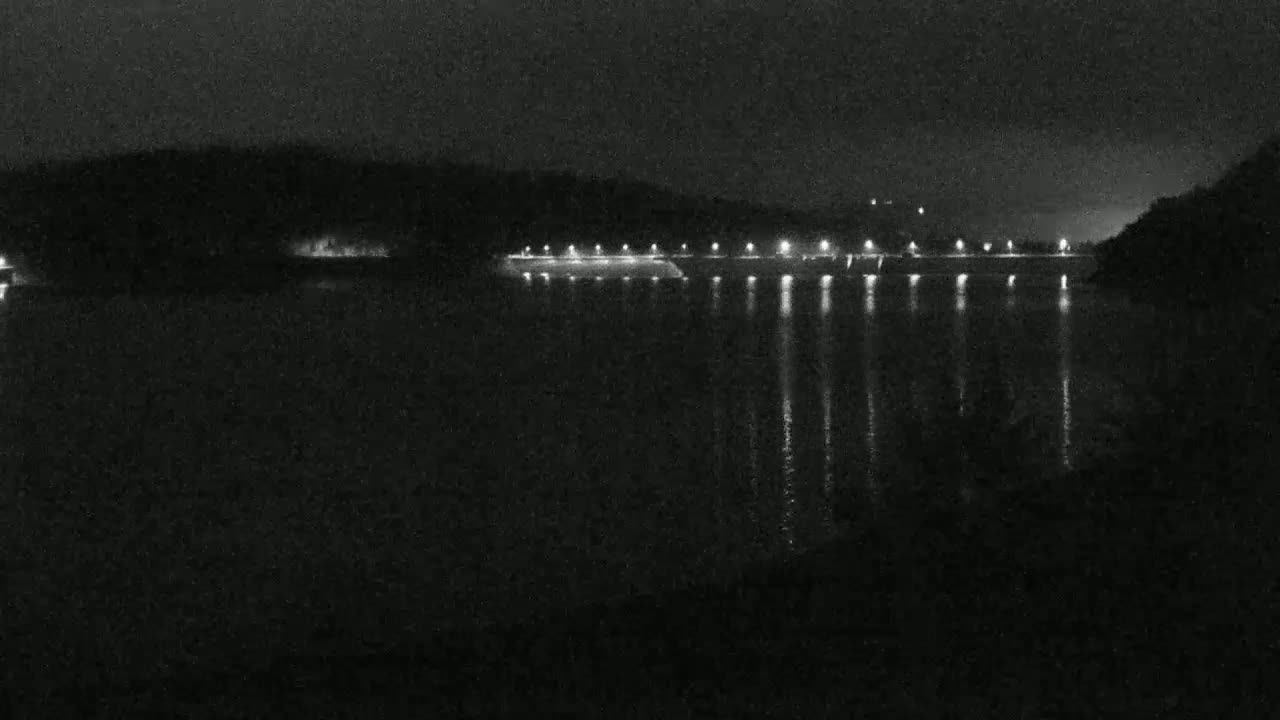 A nighttime view of a body of water reflecting the lights of a structure along its shore, under a dark sky.
