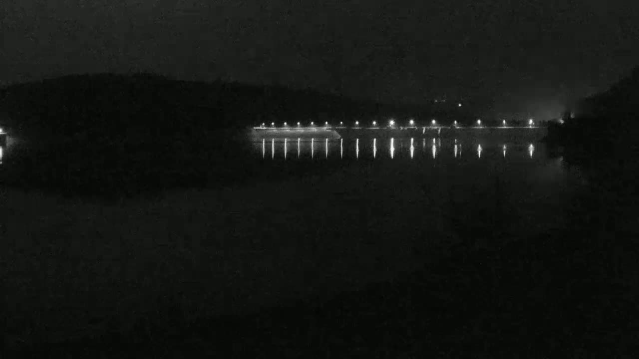 At night, a line of lights reflects on a dark body of water next to a dark shoreline.