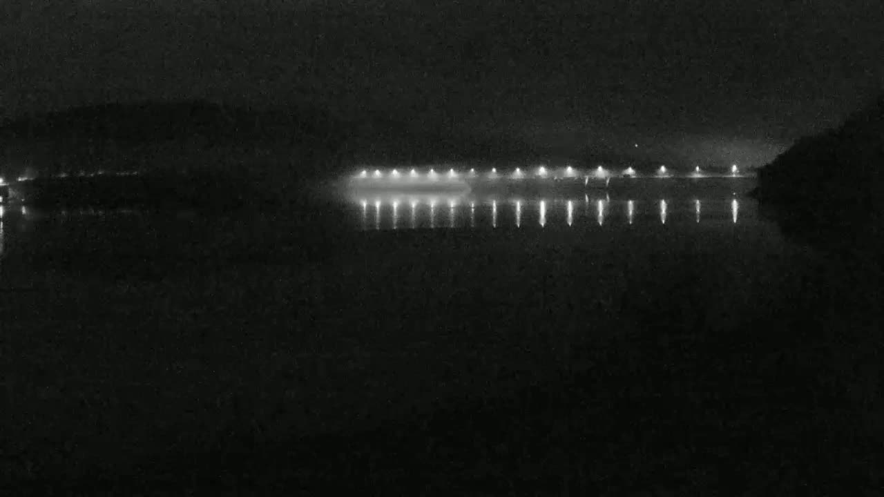 Lights from a structure illuminate a dark, still body of water at night.