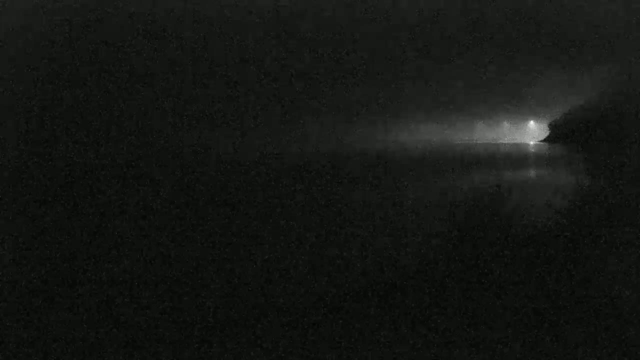 A nighttime, possibly foggy, scene shows a faint light source on a body of water.