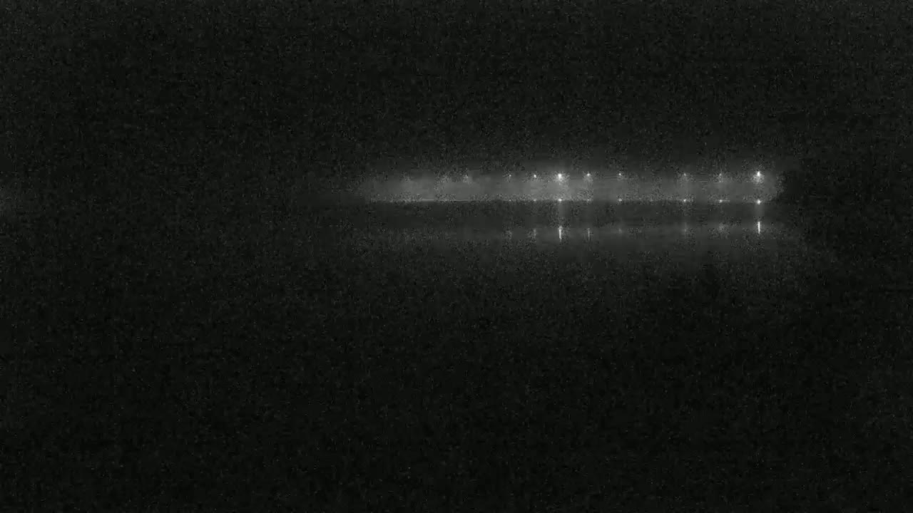 A dimly lit structure with lights is reflected in dark, still water at night.