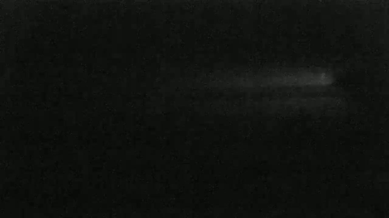 A faint, horizontal streak of light appears across a predominantly dark, textured background under a night sky.