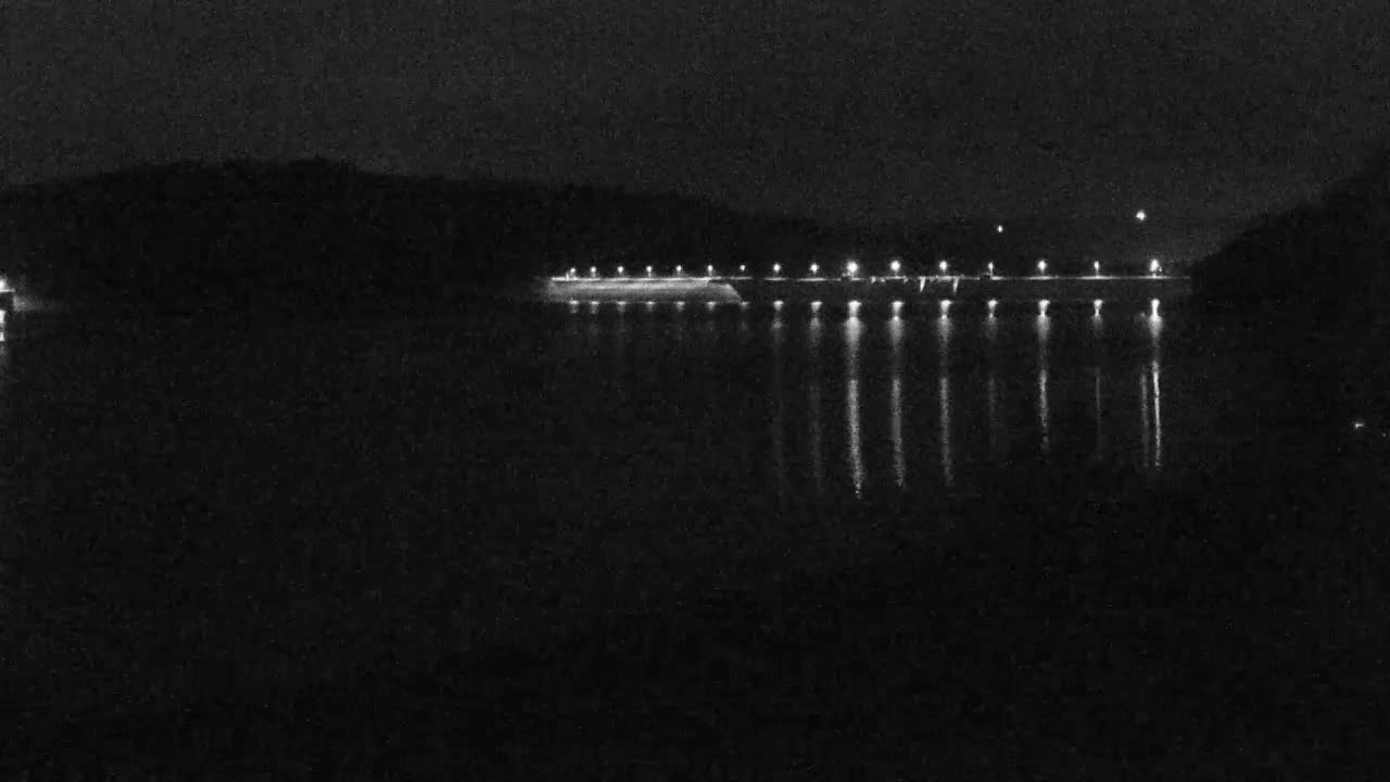 At night, a long, low structure with lights is reflected in calm water.