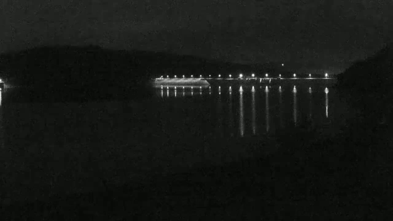 A dark, calm body of water reflects the lights of a structure on the far shore at night.