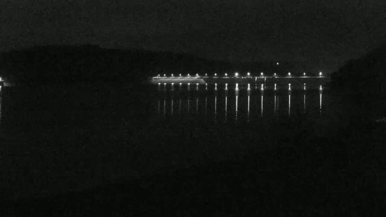 A dark, still body of water reflects the lights of a structure on the far shore at night.