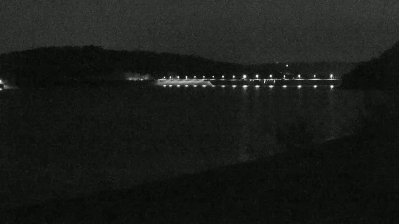 A long, dark structure with lights is visible across a body of water at night.