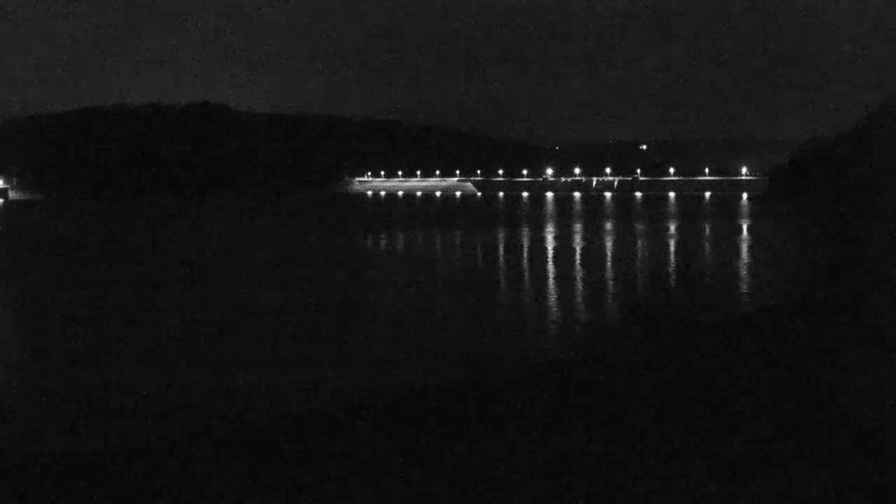 A nighttime view of a calm body of water reflecting the lights of a dam.