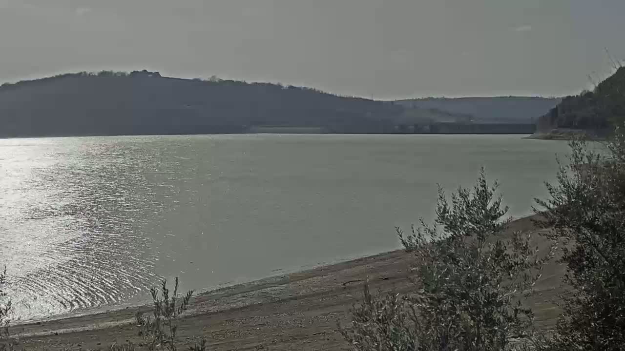 A calm body of water stretches to a distant hilly shoreline under a pale sky.